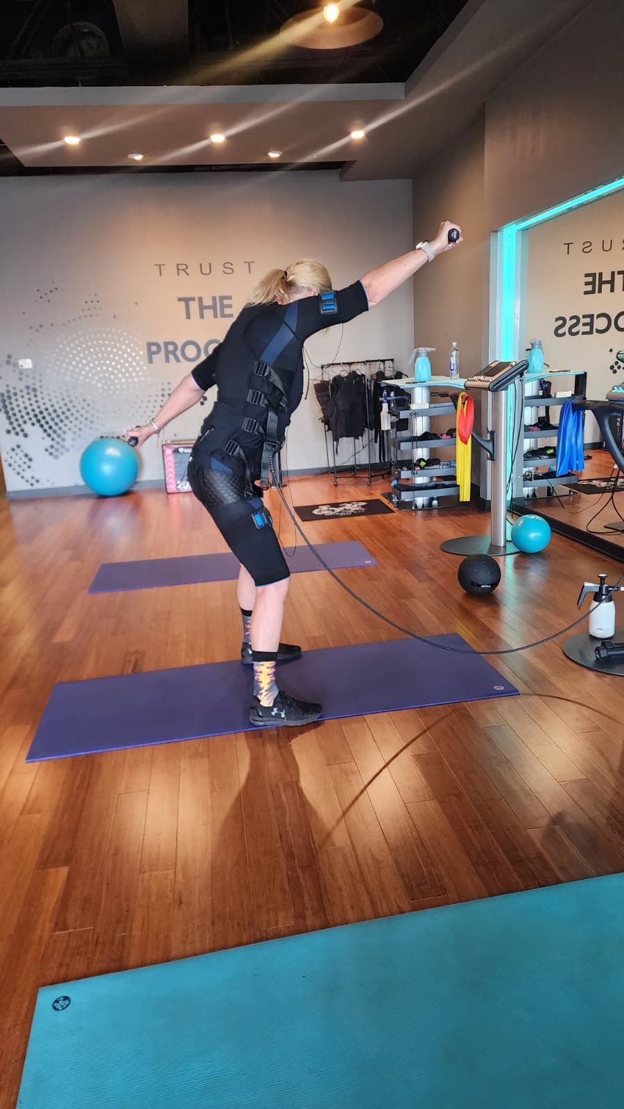 Person balancing on one leg in a gym, reaching upward on a yoga mat amid exercise equipment