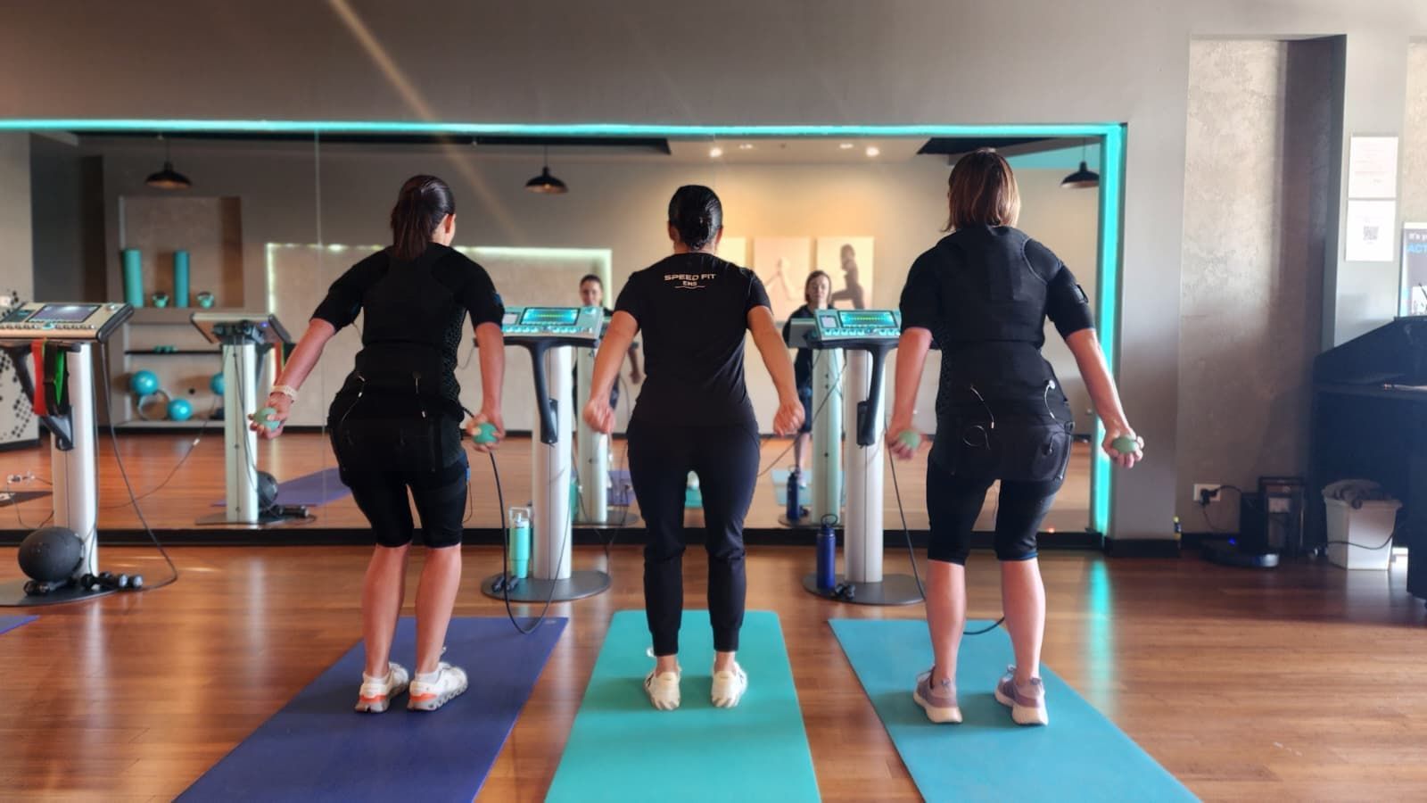 Three people doing a workout on yoga mats in a mirrored gym studio.