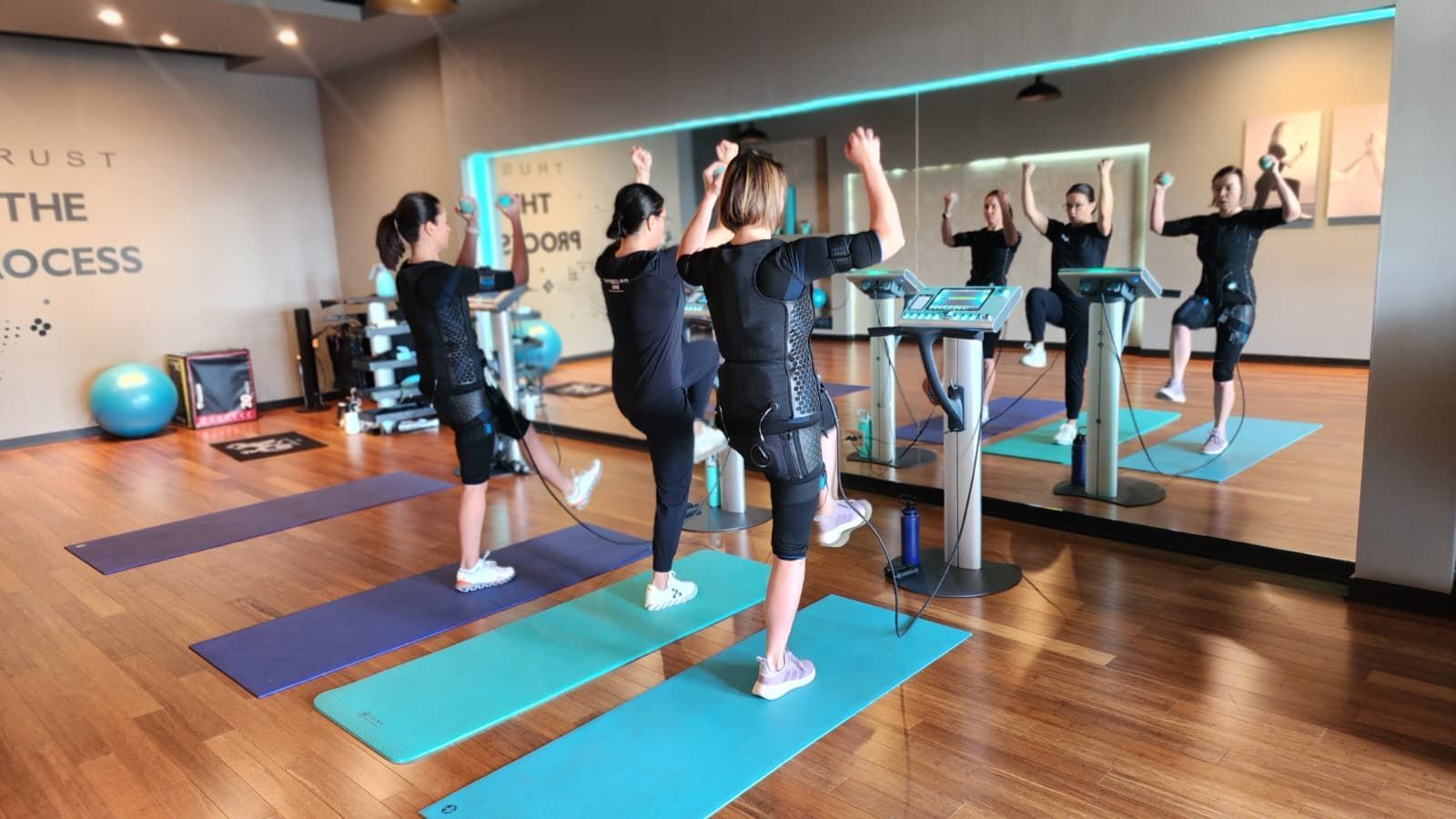 People exercising on treadmills and yoga mats in a bright studio with mirrors and wood floors