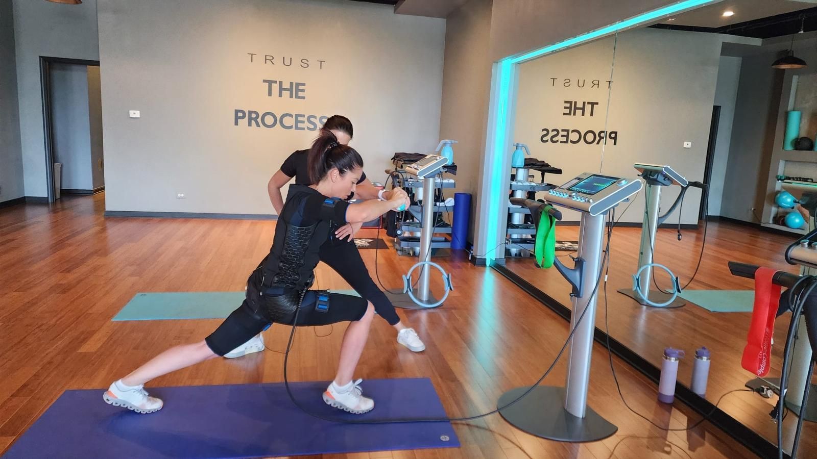 Person lunging on a mat in a gym studio, with exercise equipment and mirrored walls behind them.