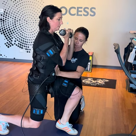 Woman in EMS training gear kneels as another holds a dumbbell in a fitness studio.