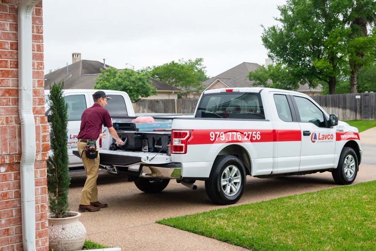 Man loading truck bed in a driveway. White service truck with red branding parked next to a van.