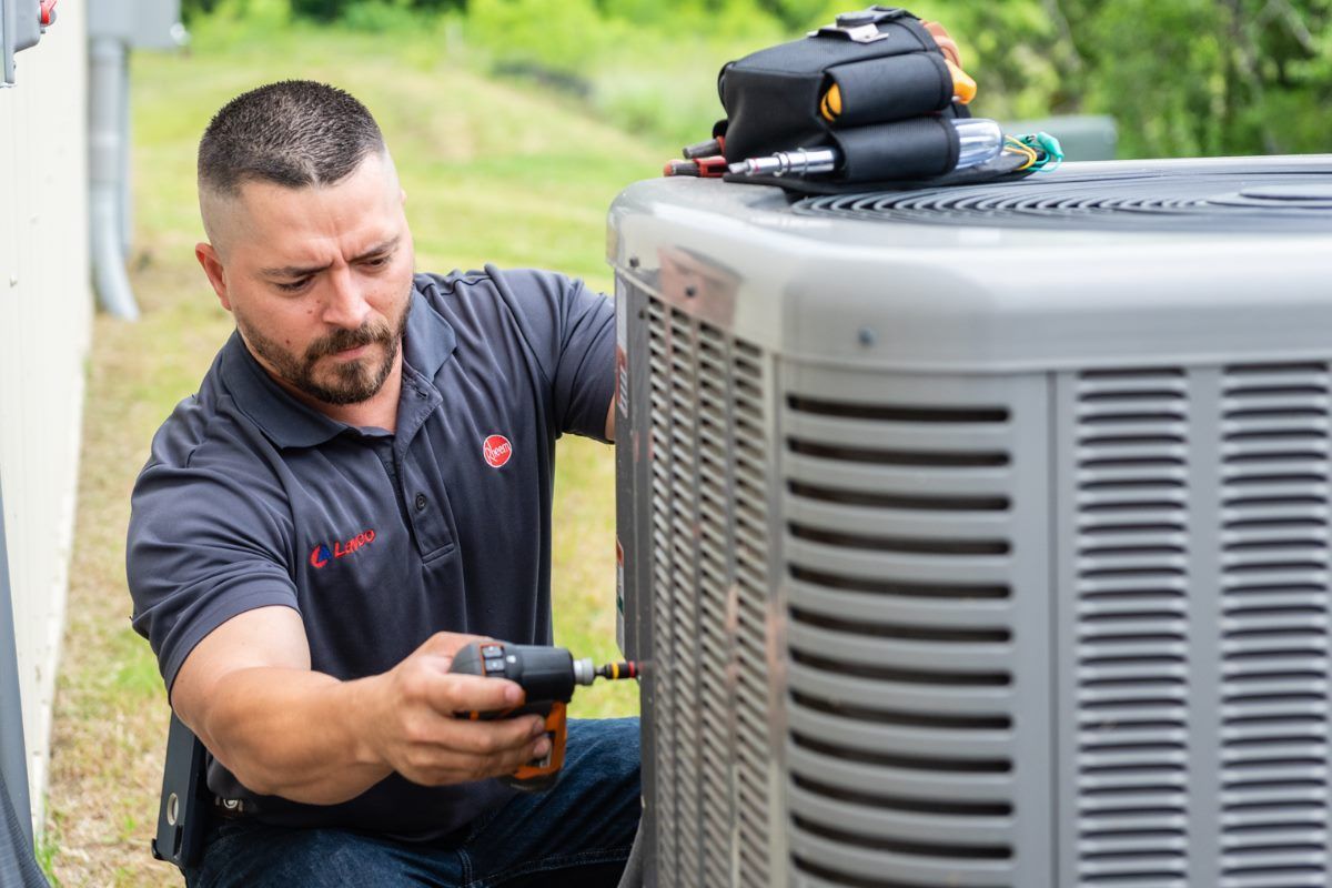 Man working on an AC unit outdoors with a screwdriver.