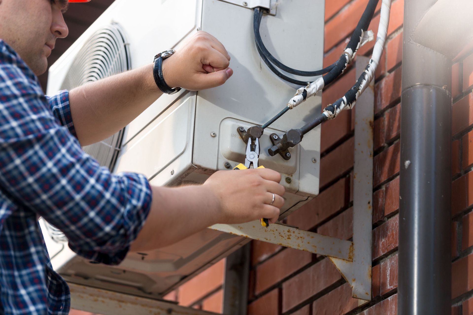 HVAC technician repairs an outdoor air conditioning unit on a brick wall.
