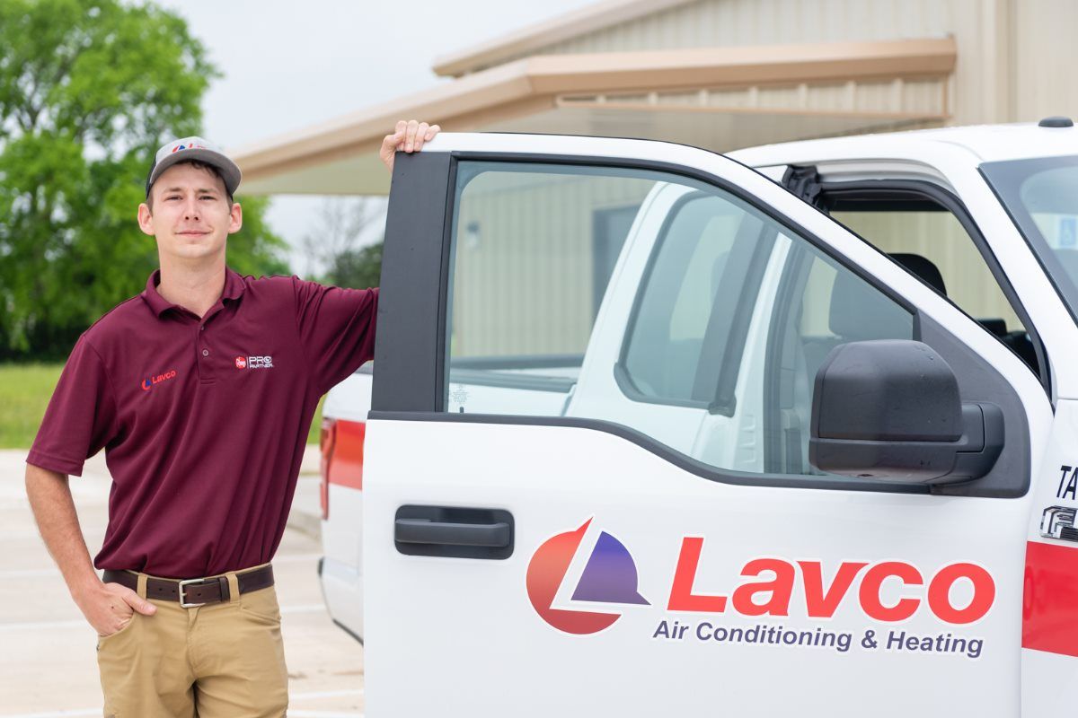 Man in maroon shirt, standing by a white Lavco truck. The truck door is open.