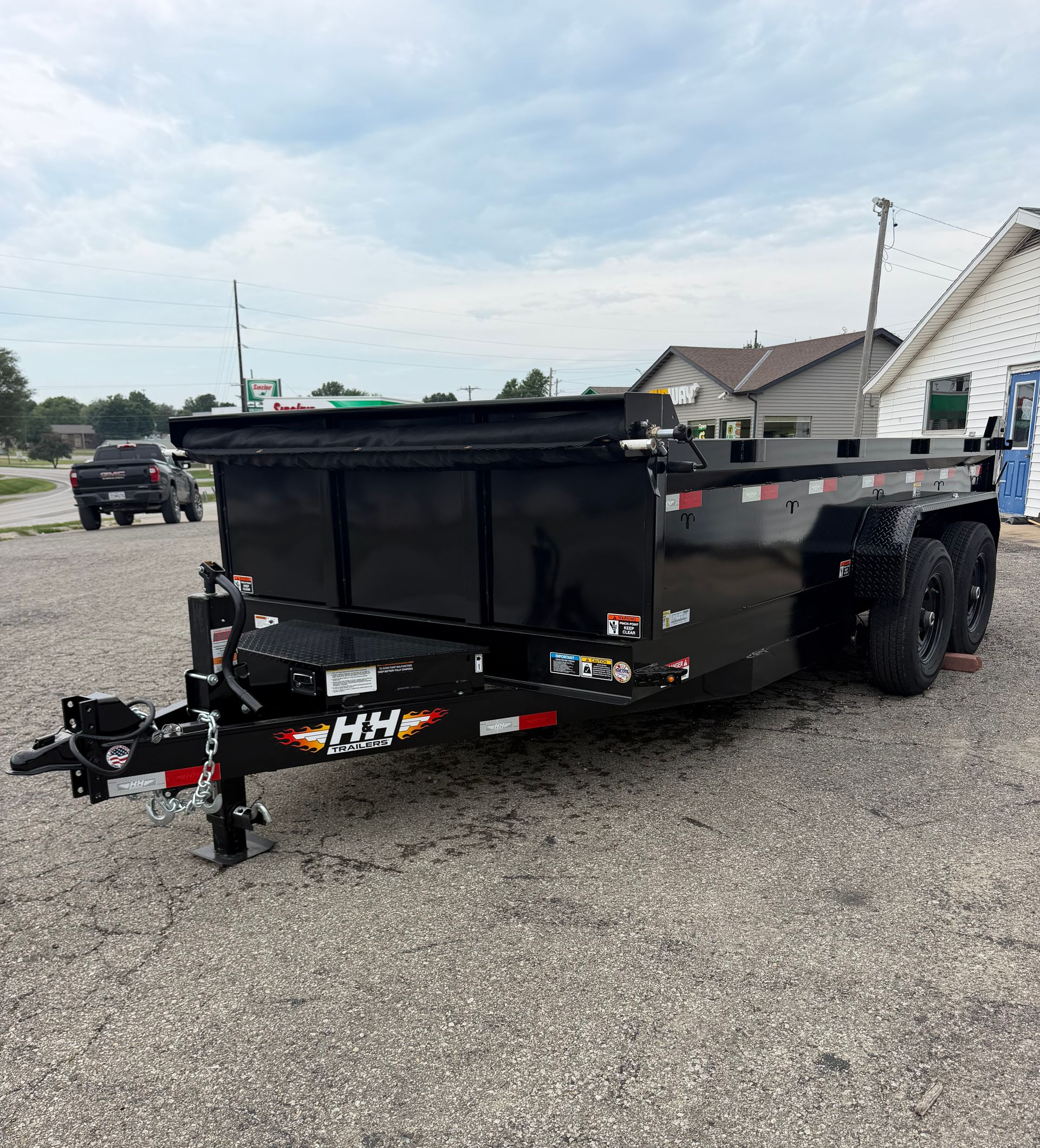 Black dump trailer with dual wheels, parked on gravel