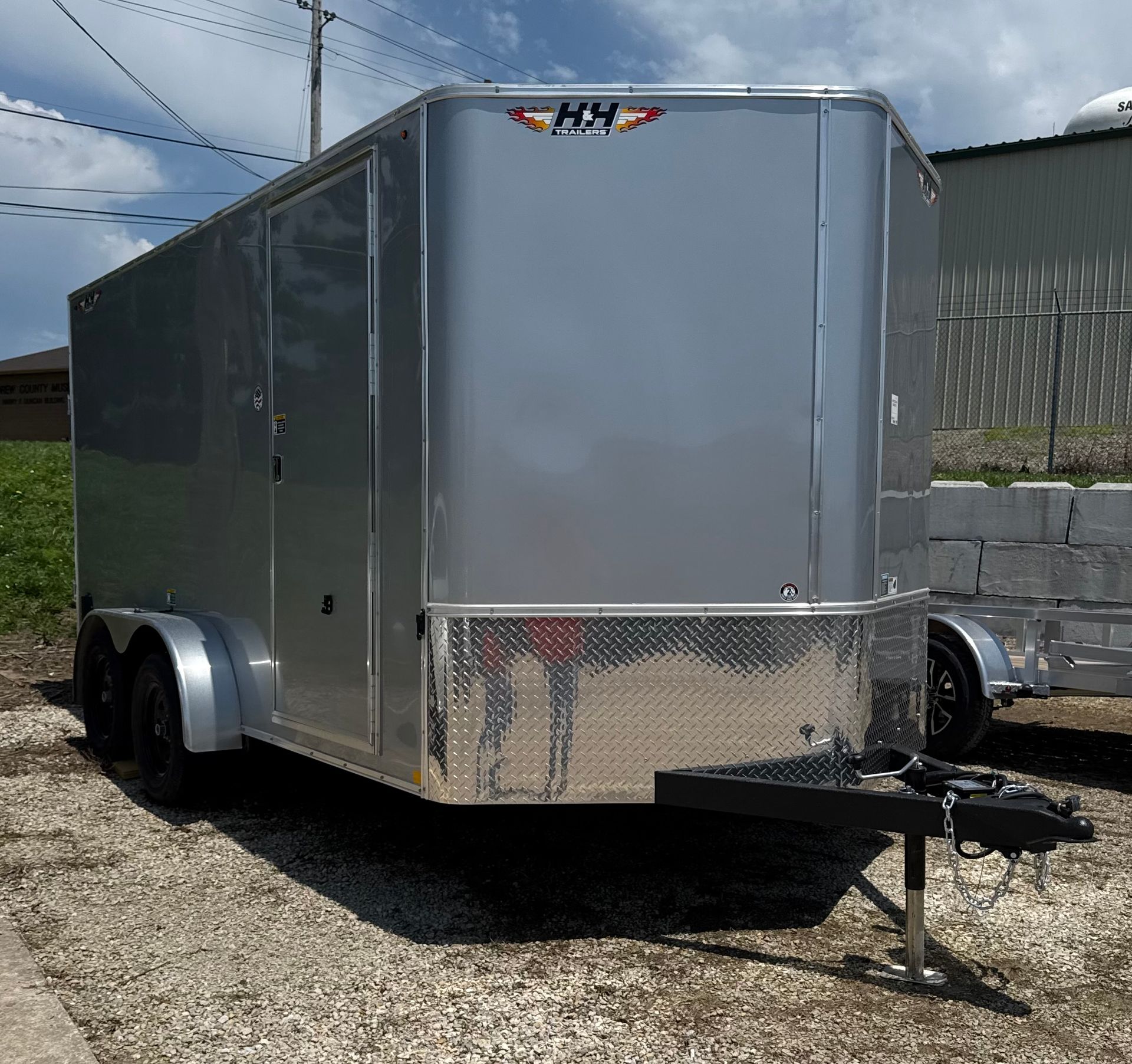 Gray enclosed cargo trailer with black wheels, door, and a sunny outdoor setting