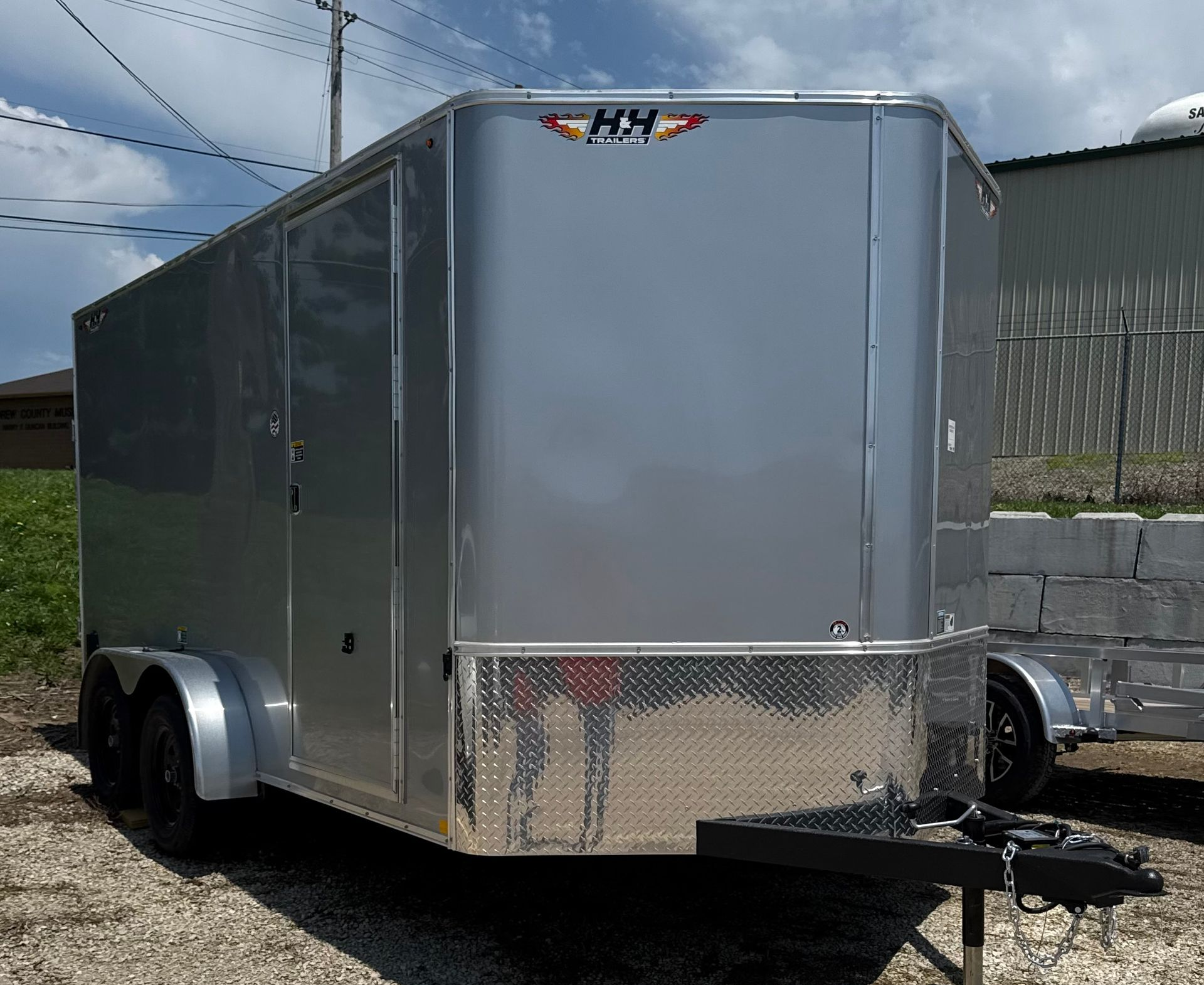 Gray enclosed cargo trailer with black wheels, door, and a sunny outdoor setting