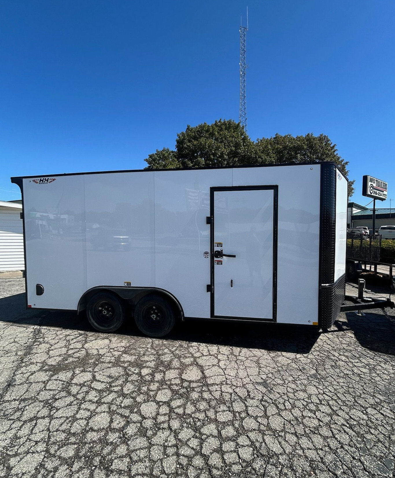 White enclosed cargo trailer on a paved lot with a parked truck in the background