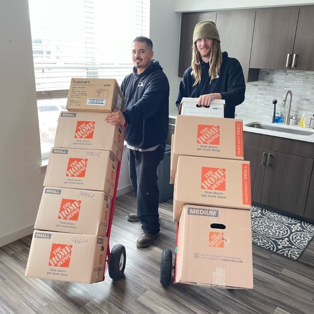 Two men are carrying boxes on a dolly in a kitchen.