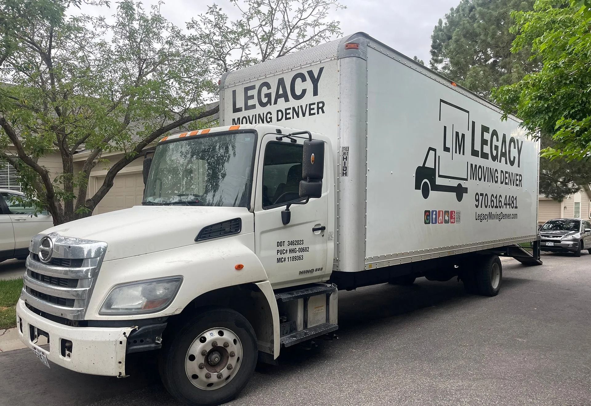 A white legacy moving truck is parked in front of a house.