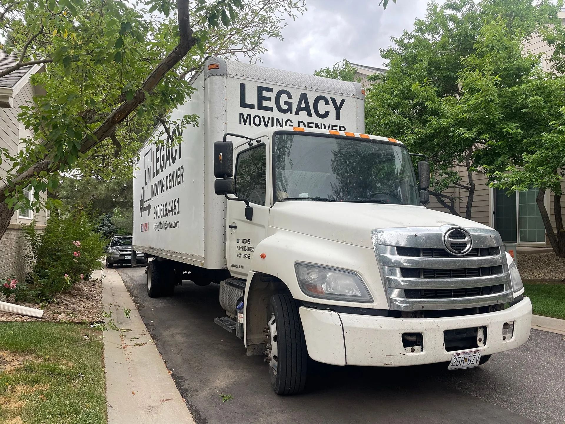 A white legacy moving truck is parked in front of a house.