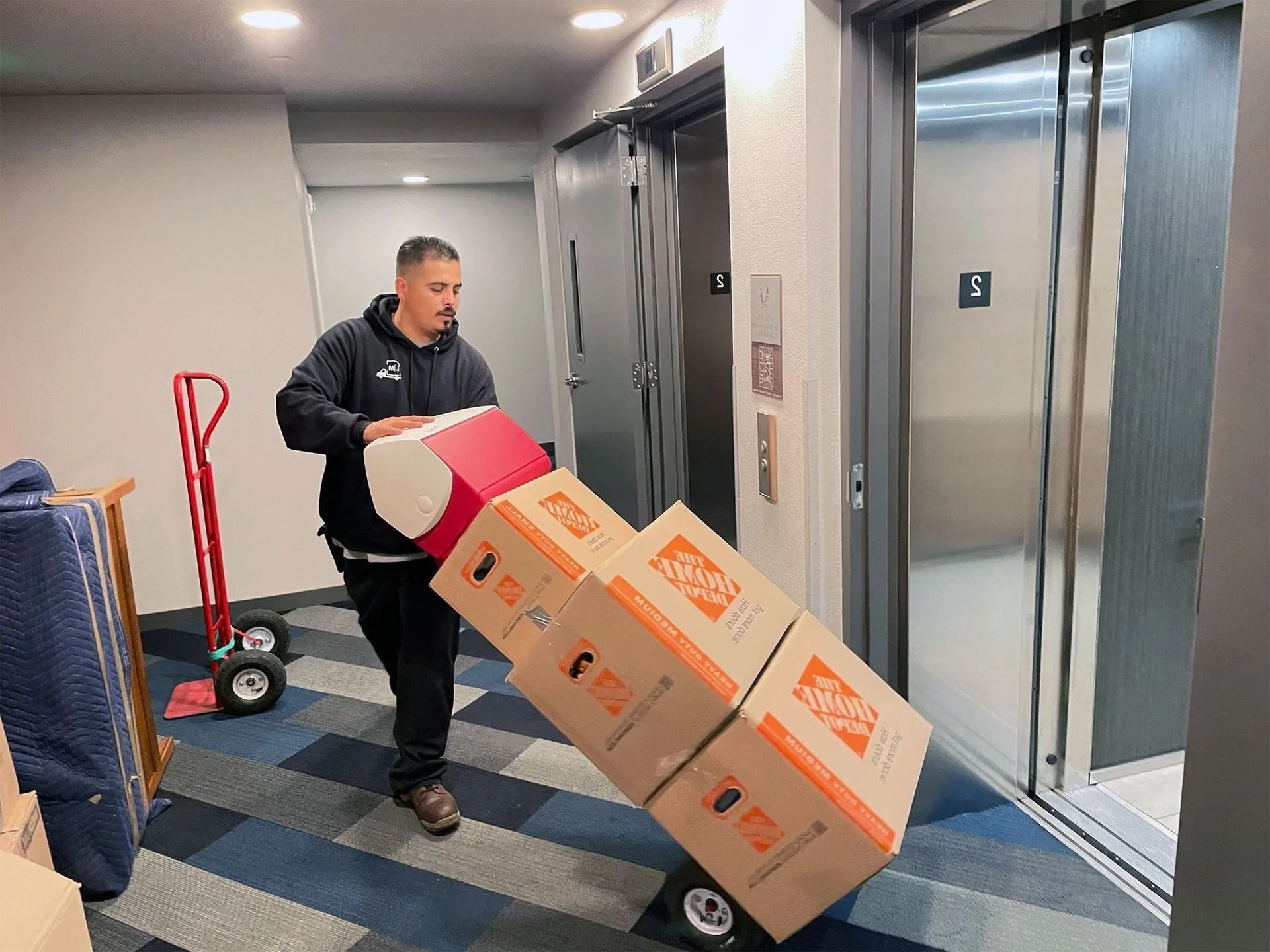 A man is carrying boxes on a dolly into an elevator.
