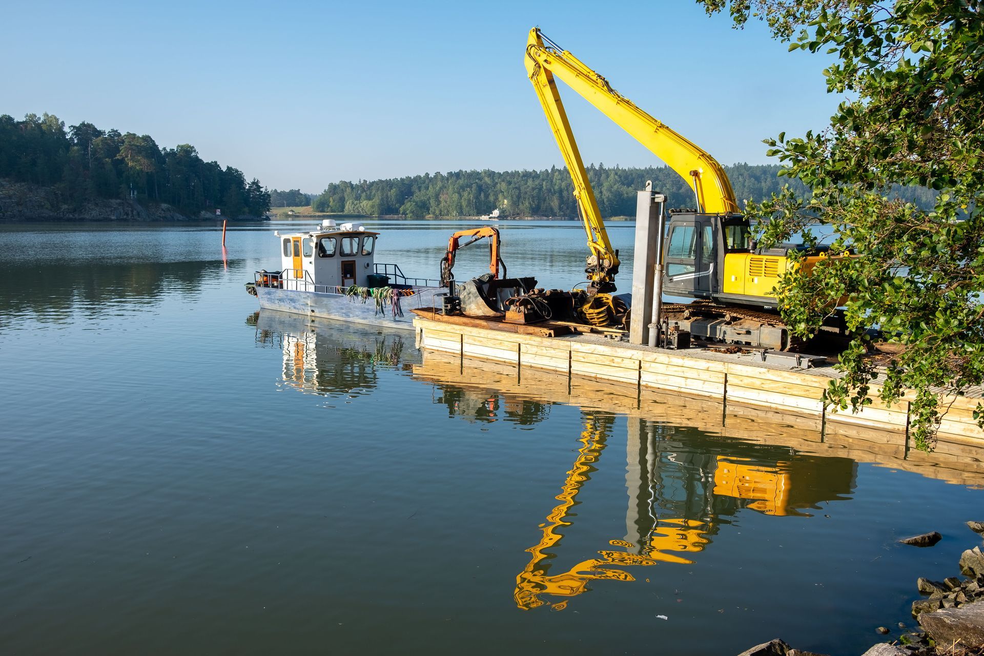 A yellow excavator is working on a boat in the water