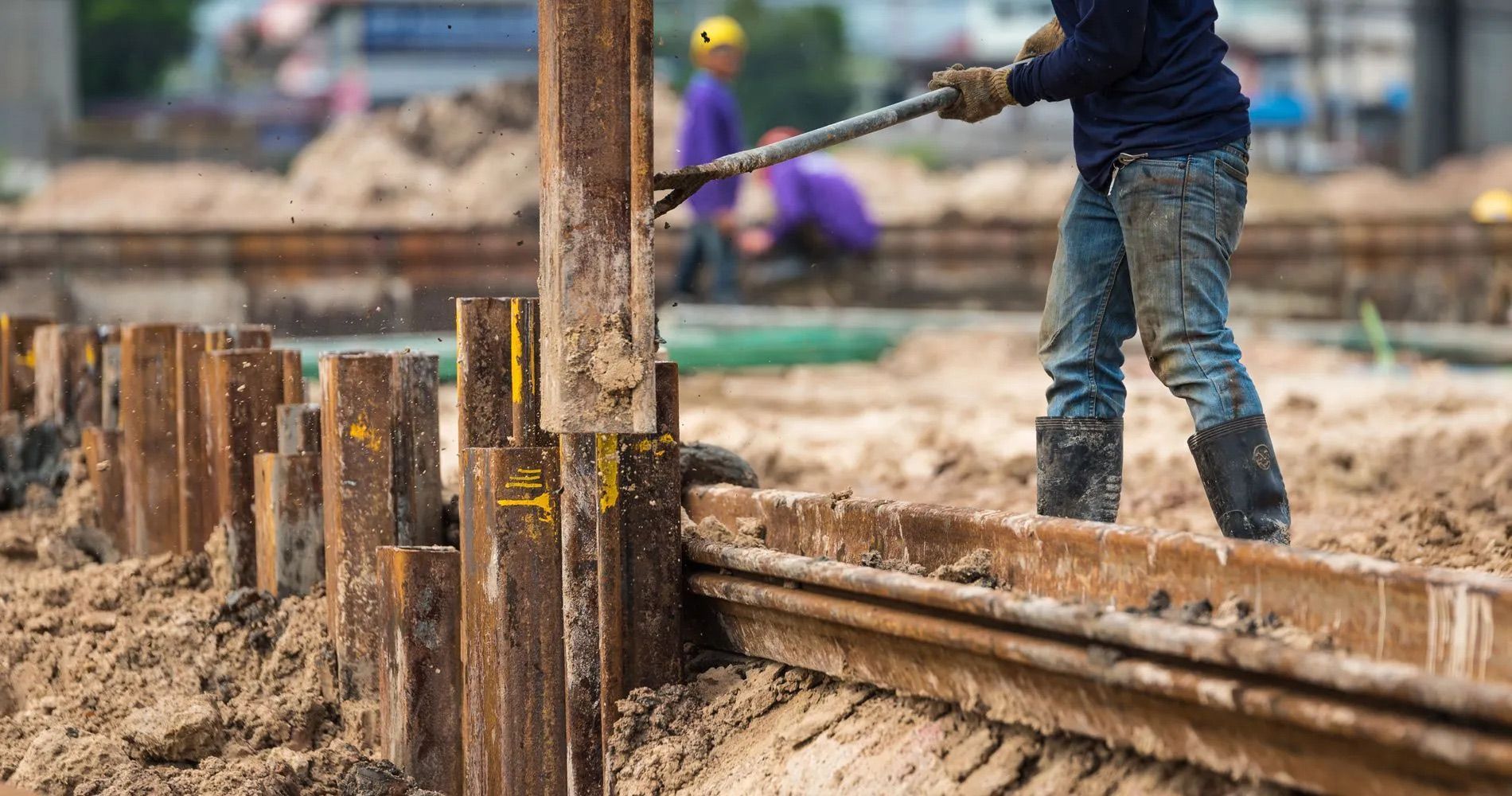 A construction worker is using a hammer to hammer a metal pole at a construction site.