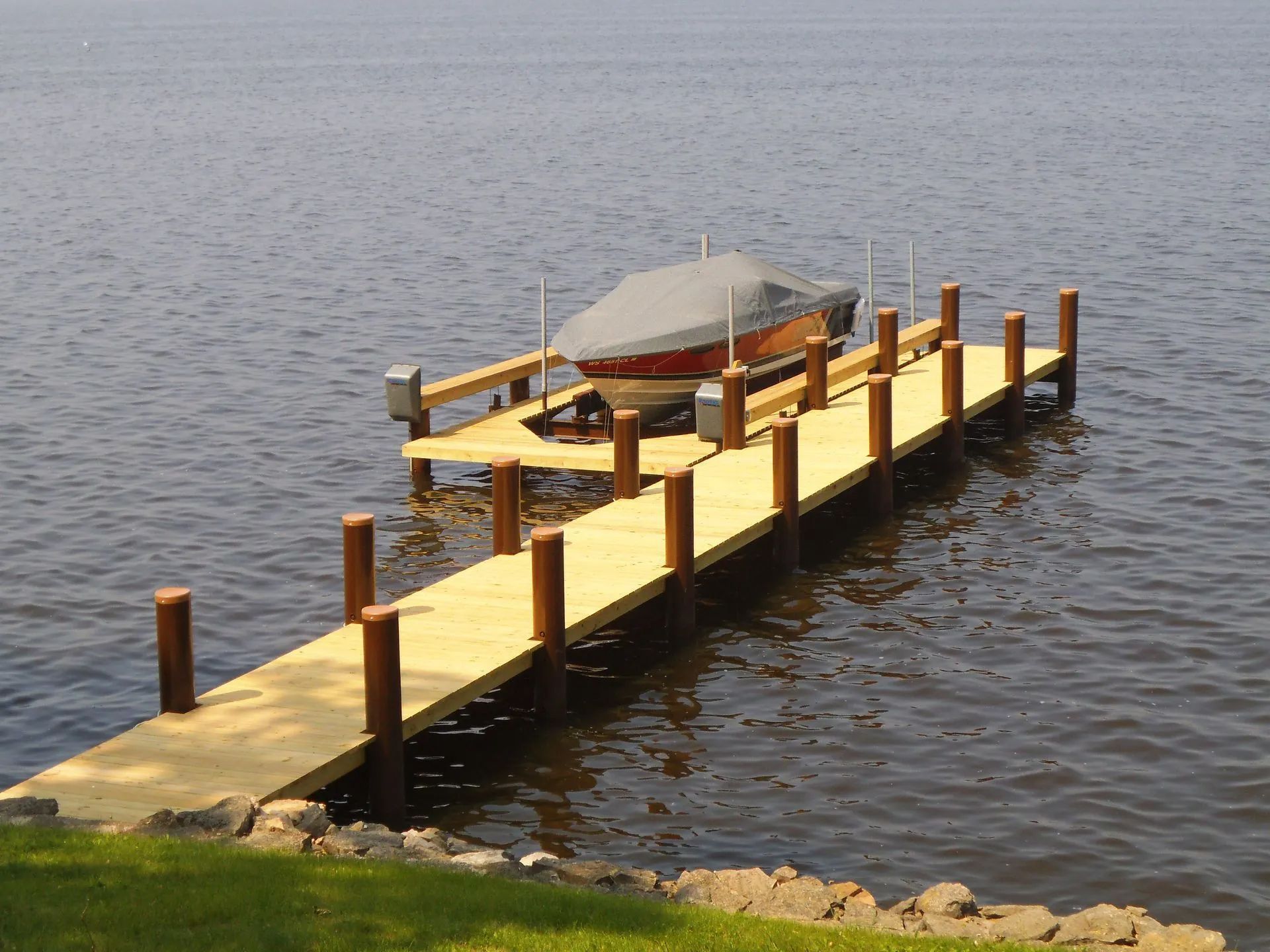 Wooden dock with a covered boat on a lift, brown posts, and a lake in the background.