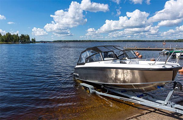 A boat is docked on a trailer on the shore of a lake.