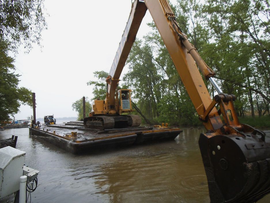 A large yellow excavator is on a boat in the water