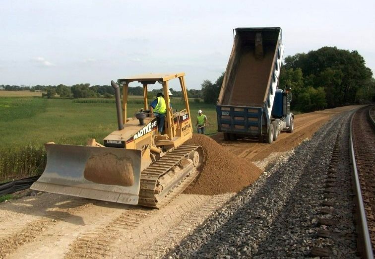 A bulldozer is moving dirt next to a dump truck