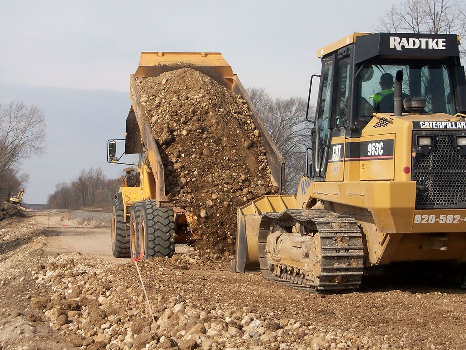 A bulldozer is loading dirt into a dump truck