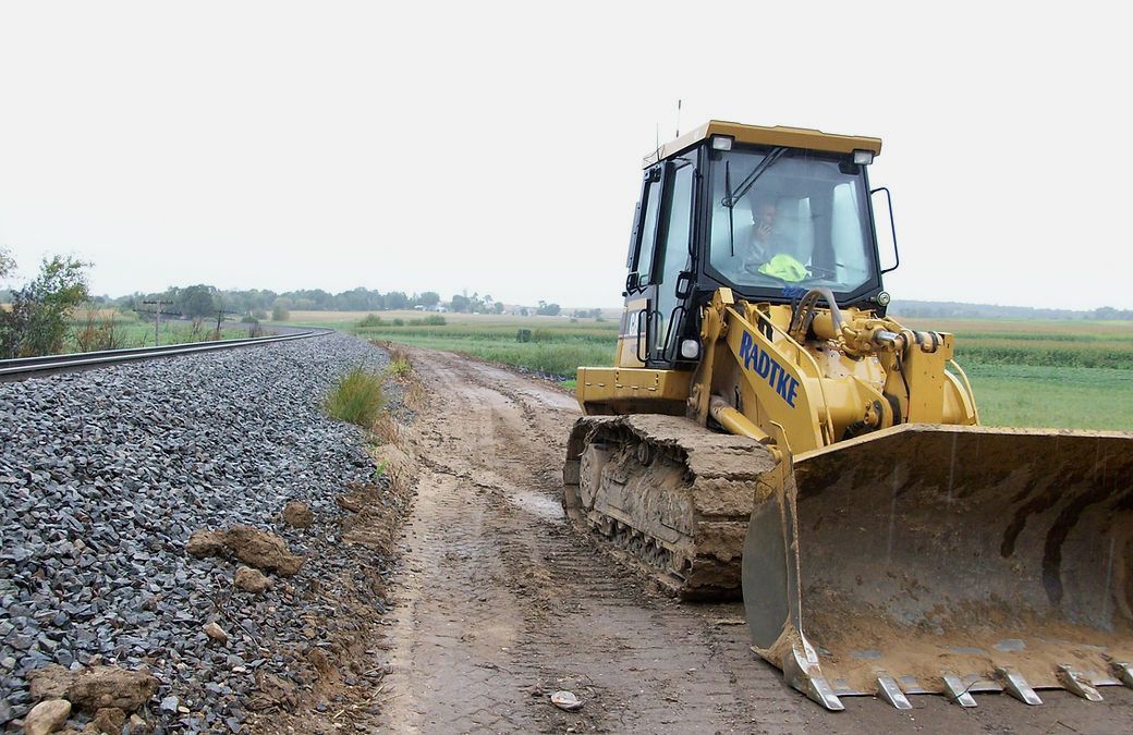 A bulldozer is driving down a dirt road next to train tracks.