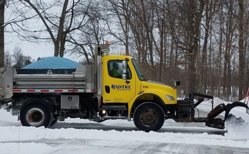 A yellow truck with a plow attached to it is parked in the snow.