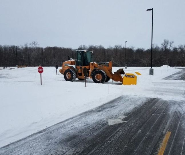 A snow plow is clearing snow from a parking lot