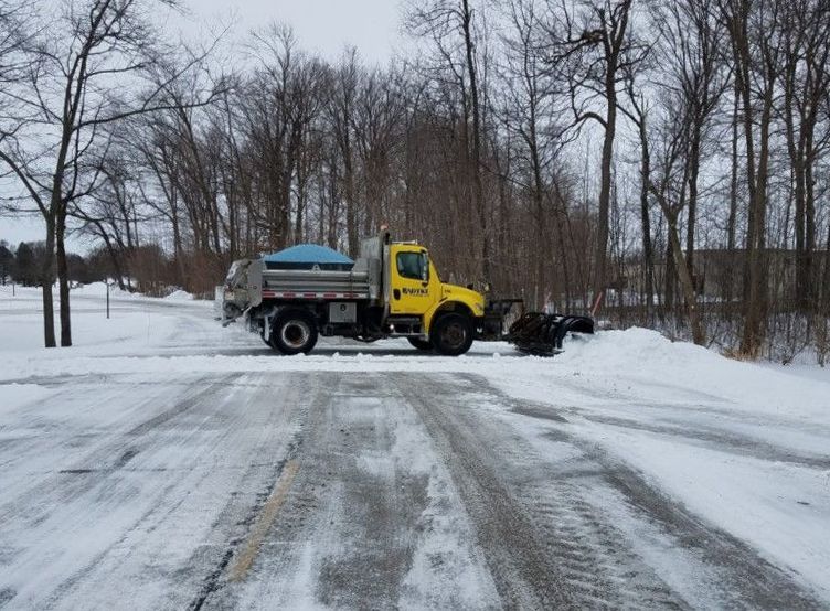A yellow truck is plowing snow on a snowy road.