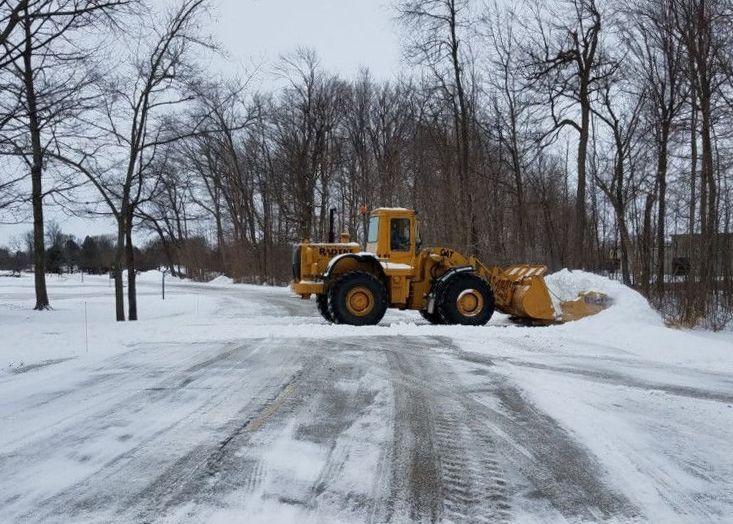 A yellow snow plow is driving down a snow covered road.