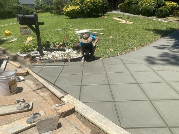 Person working on a concrete driveway. Freshly poured squares, wooden forms, and mailbox in front yard.