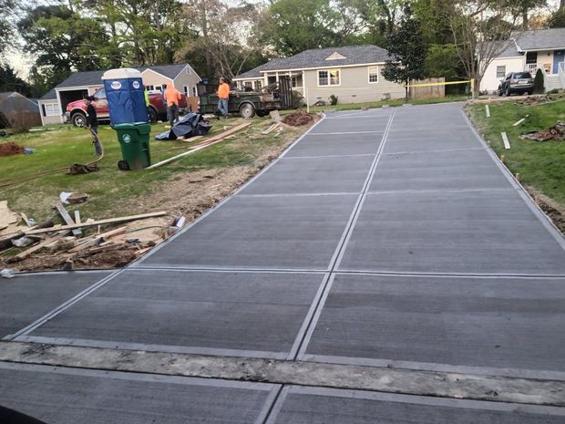Newly poured concrete driveway with workers and houses in the background.