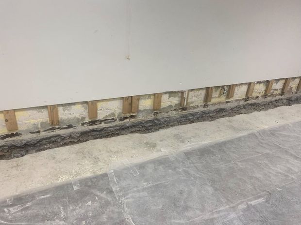 Wall under construction; exposed wooden studs below white wall; gray floor.