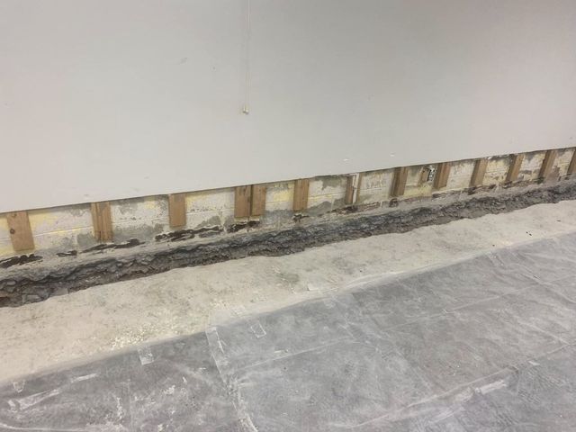 Wall under construction; exposed wooden studs below white wall; gray floor.