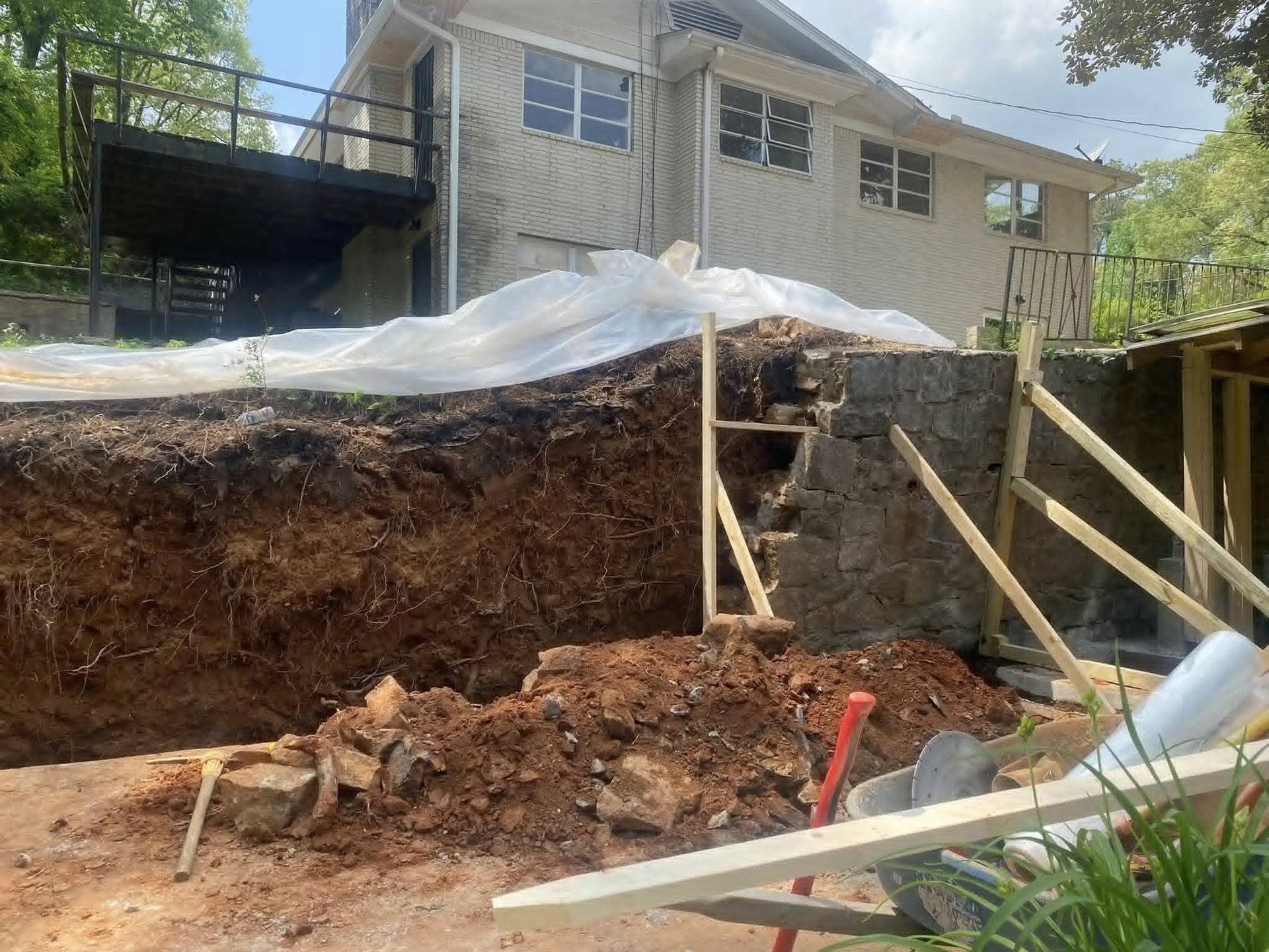 Construction site: excavated earth next to a house with a deck; supporting structure visible.