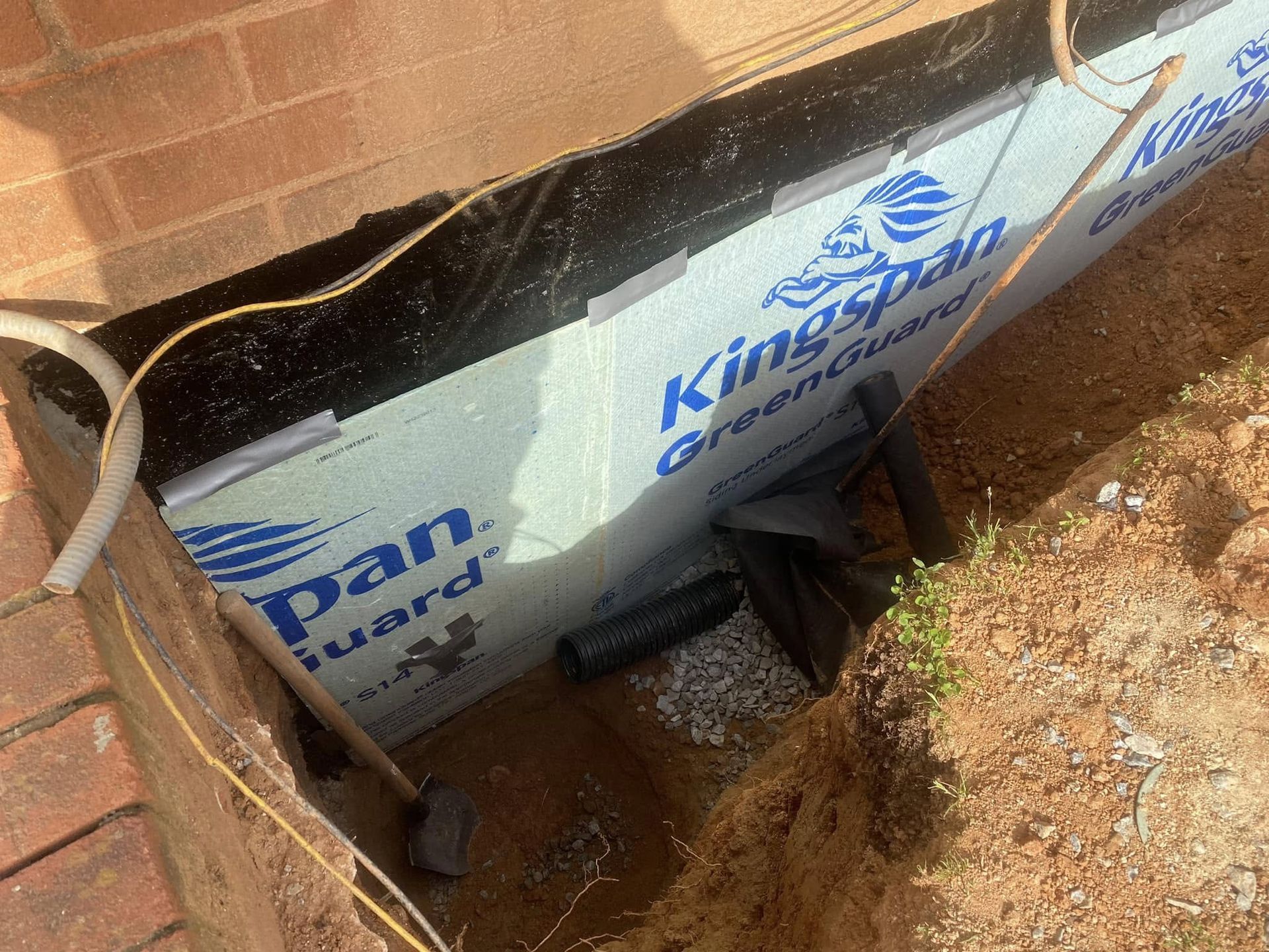 Insulated foundation wall with Kingspan panels, black membrane, and drainage pipe. Brick wall to left, outdoor setting.