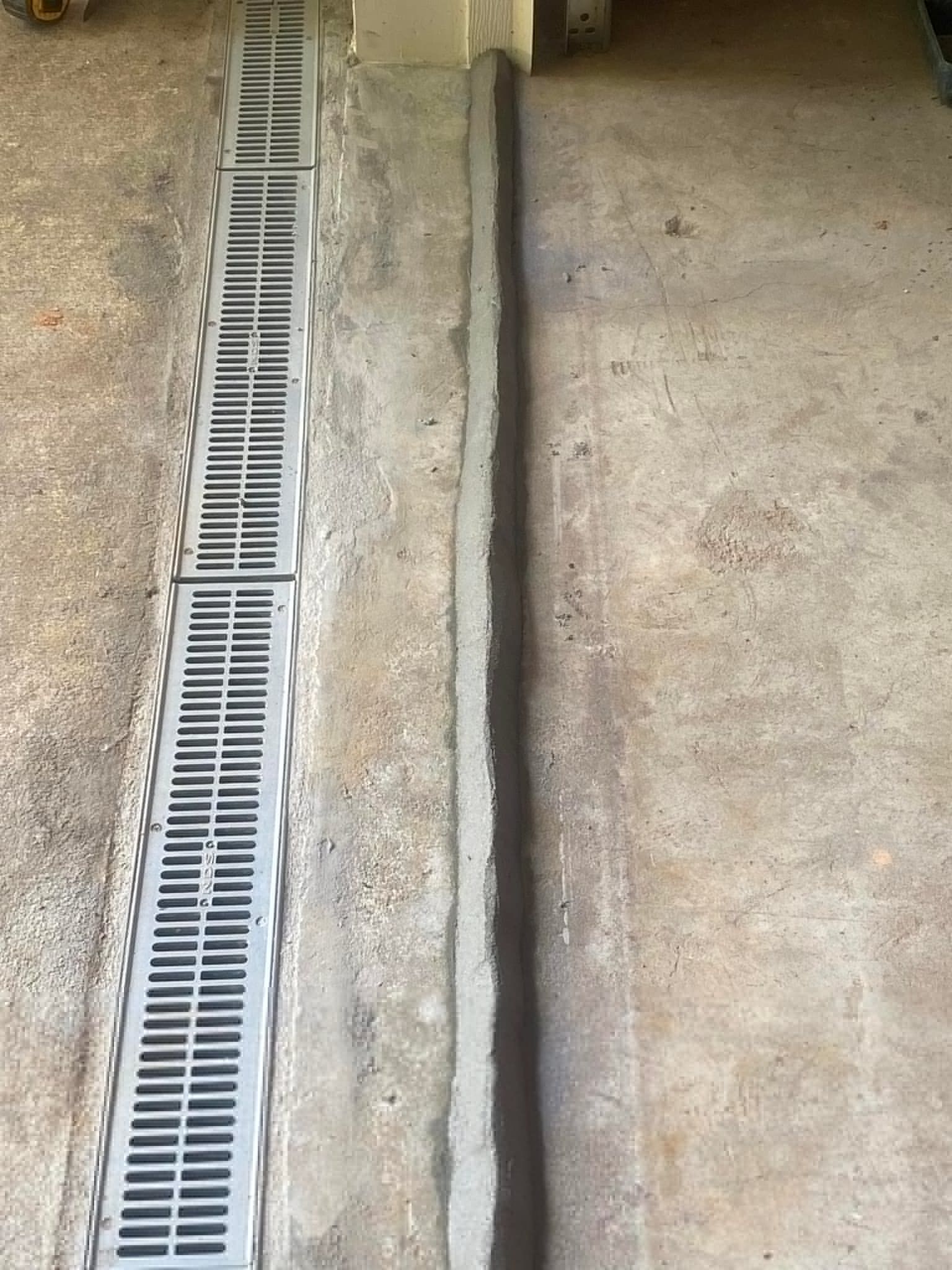 Concrete floor with a metal grate drain and a narrow raised strip of concrete running alongside it.