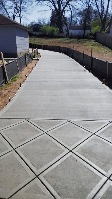 Concrete driveway with diamond pattern leading to a house, with a fence along its sides.