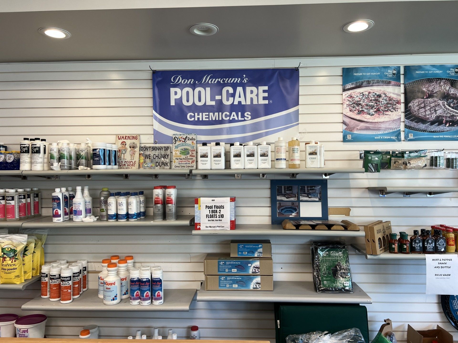 Pool-care chemicals displayed on store shelves with blue signs and various bottles and containers