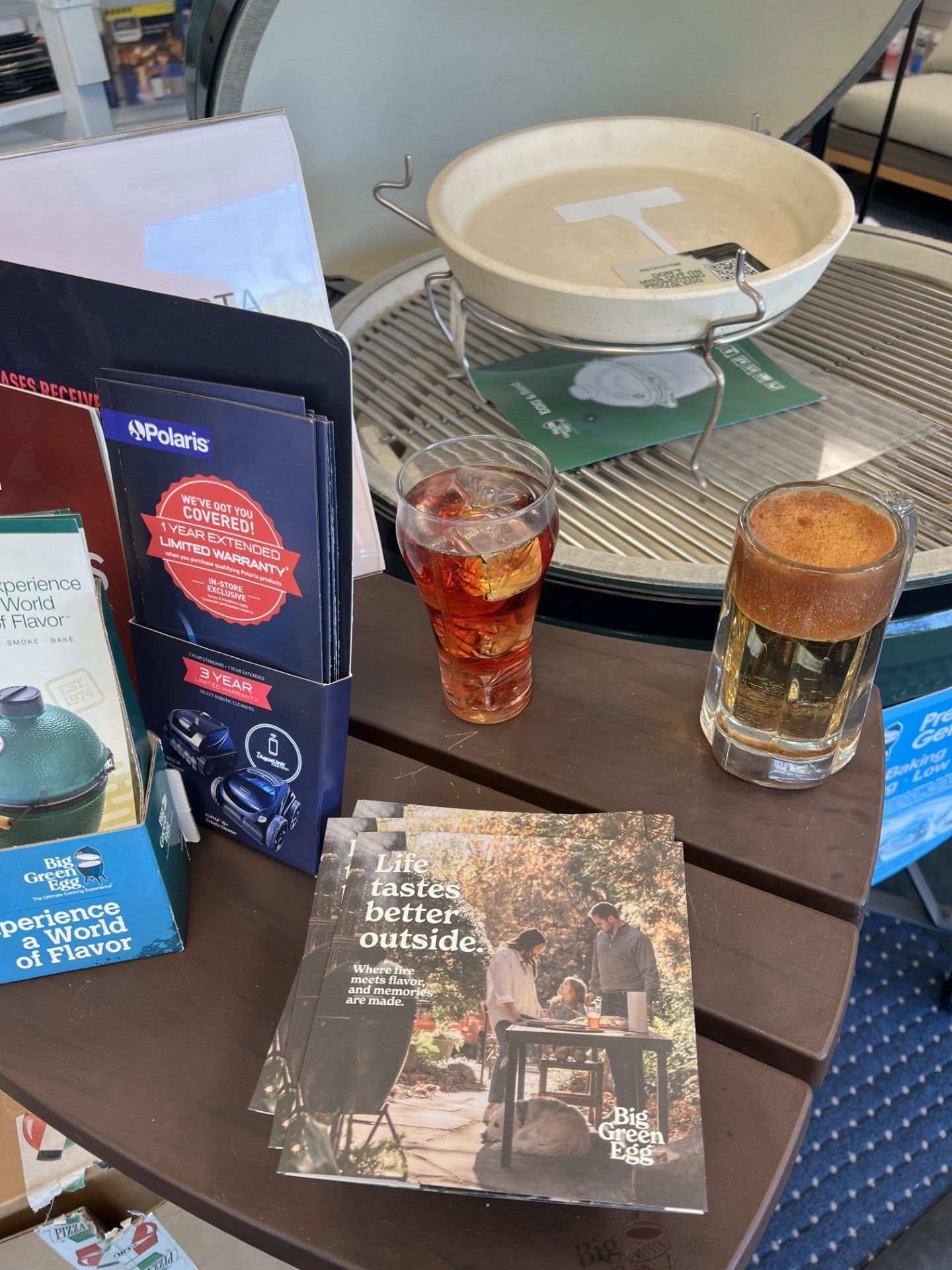 Two iced drinks on a table beside event brochures and a white bowl on a metal stand.