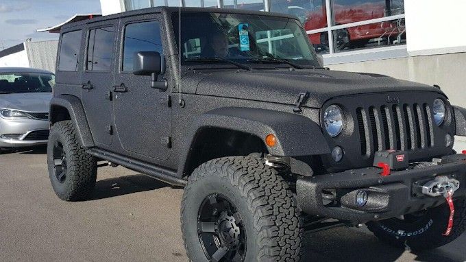 A black jeep is parked in front of a car dealership.