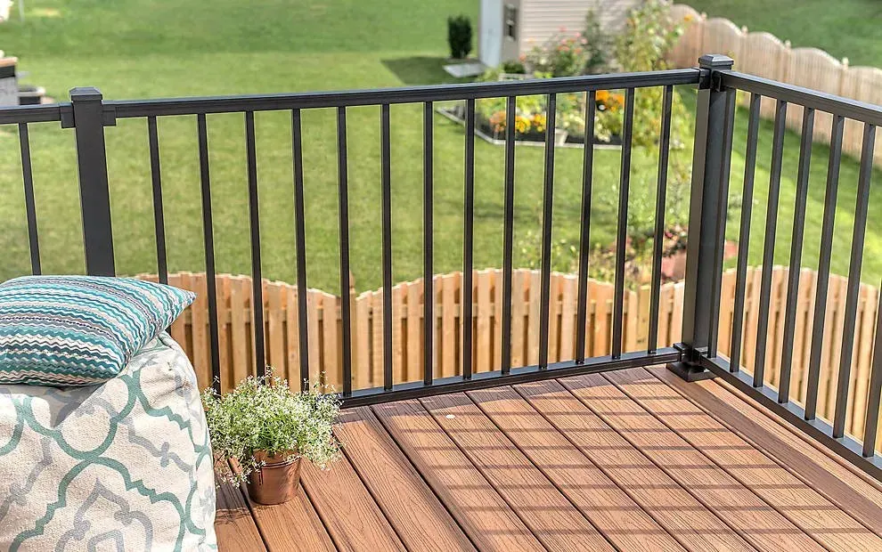 A wooden deck with a black railing and a pillow on it.