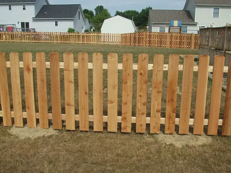 A wooden picket fence is in the middle of a grassy field