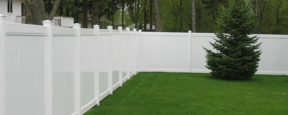 A white fence surrounds a lush green yard with a tree in the middle.