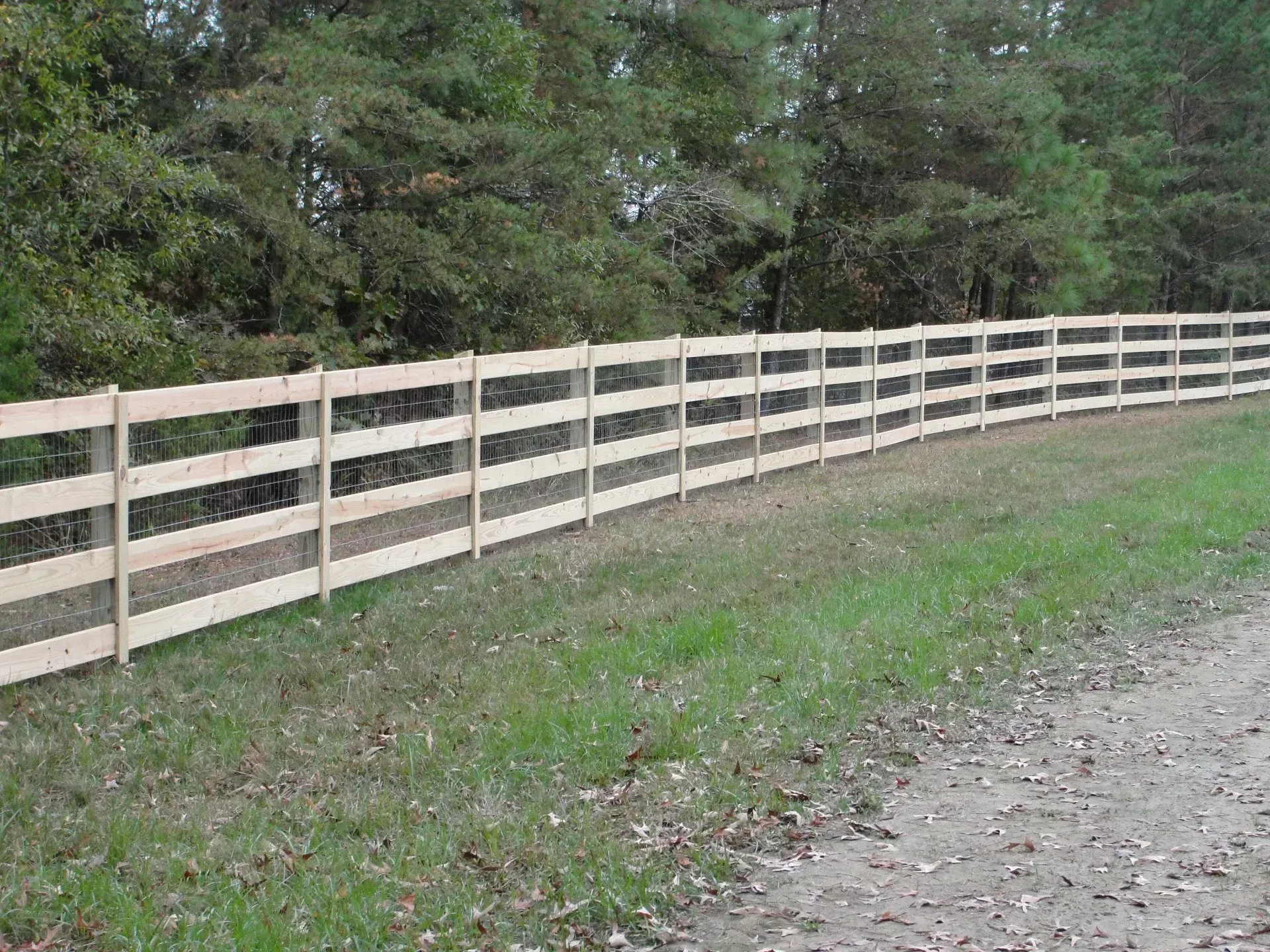 A wooden fence along a dirt road with trees in the background