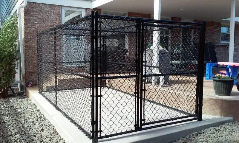A black chain link fence is sitting in front of a brick house.