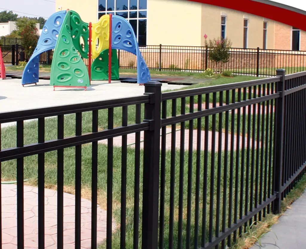 A black fence surrounds a playground with a climbing structure in the background