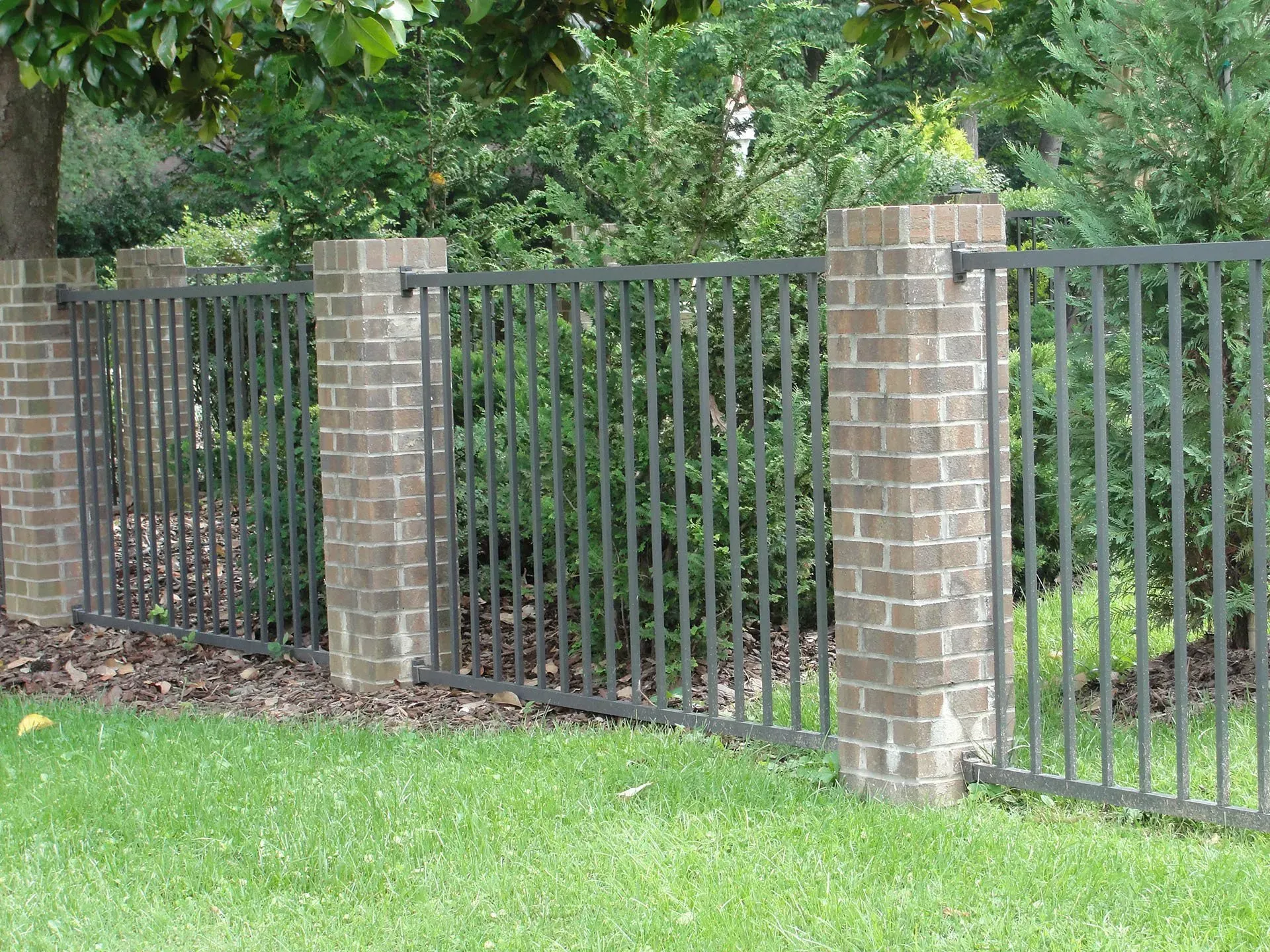 A fence made of bricks and metal is surrounded by a lush green field.