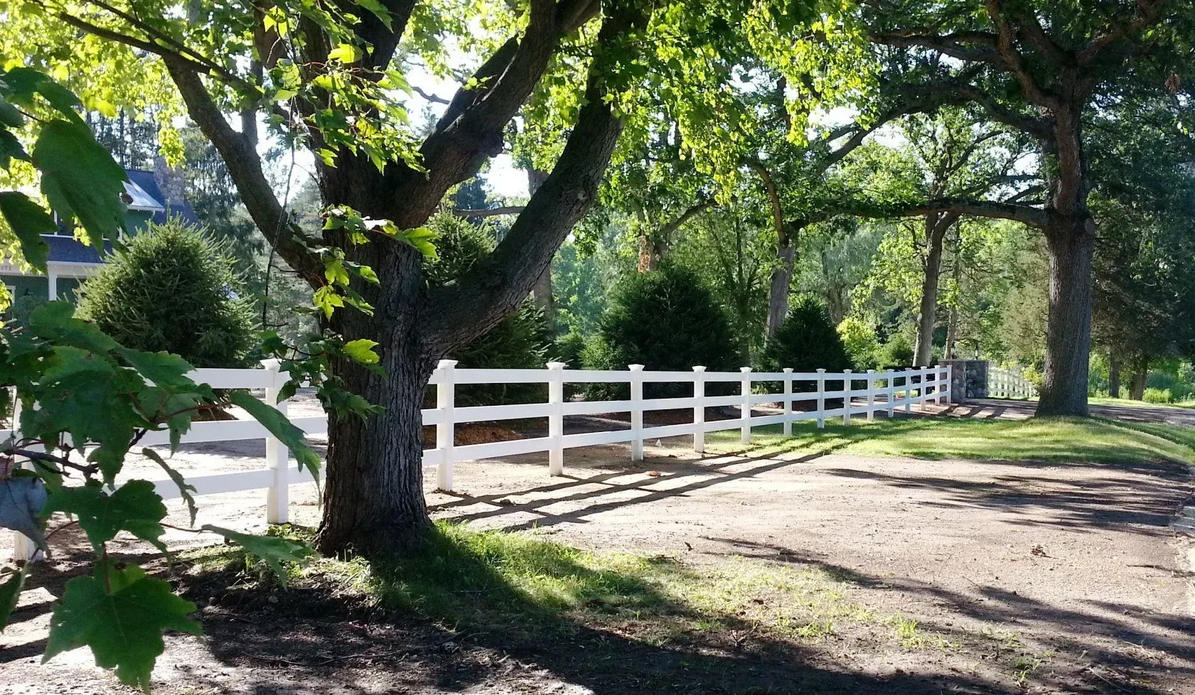 A white fence is surrounded by trees on a dirt road