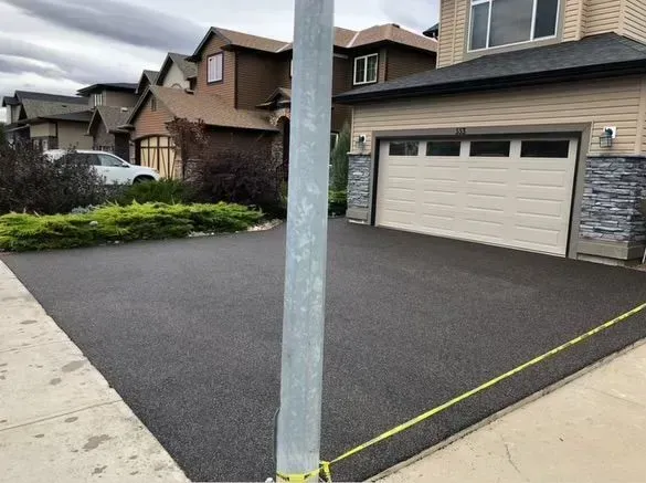Newly paved dark asphalt driveway in front of a house, with a utility pole in the foreground.