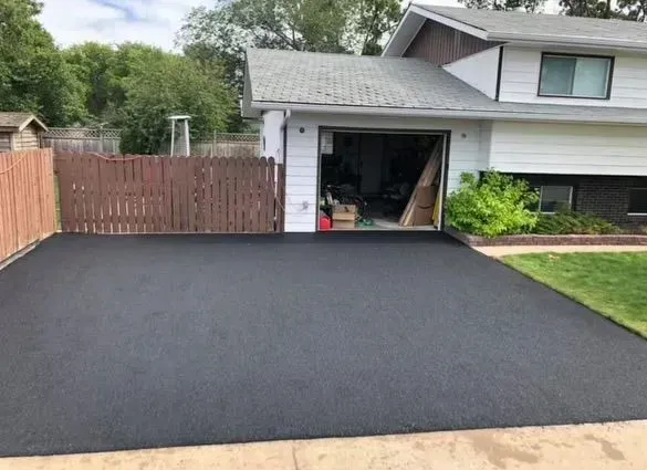 Freshly paved black asphalt driveway in front of a house with an open garage.